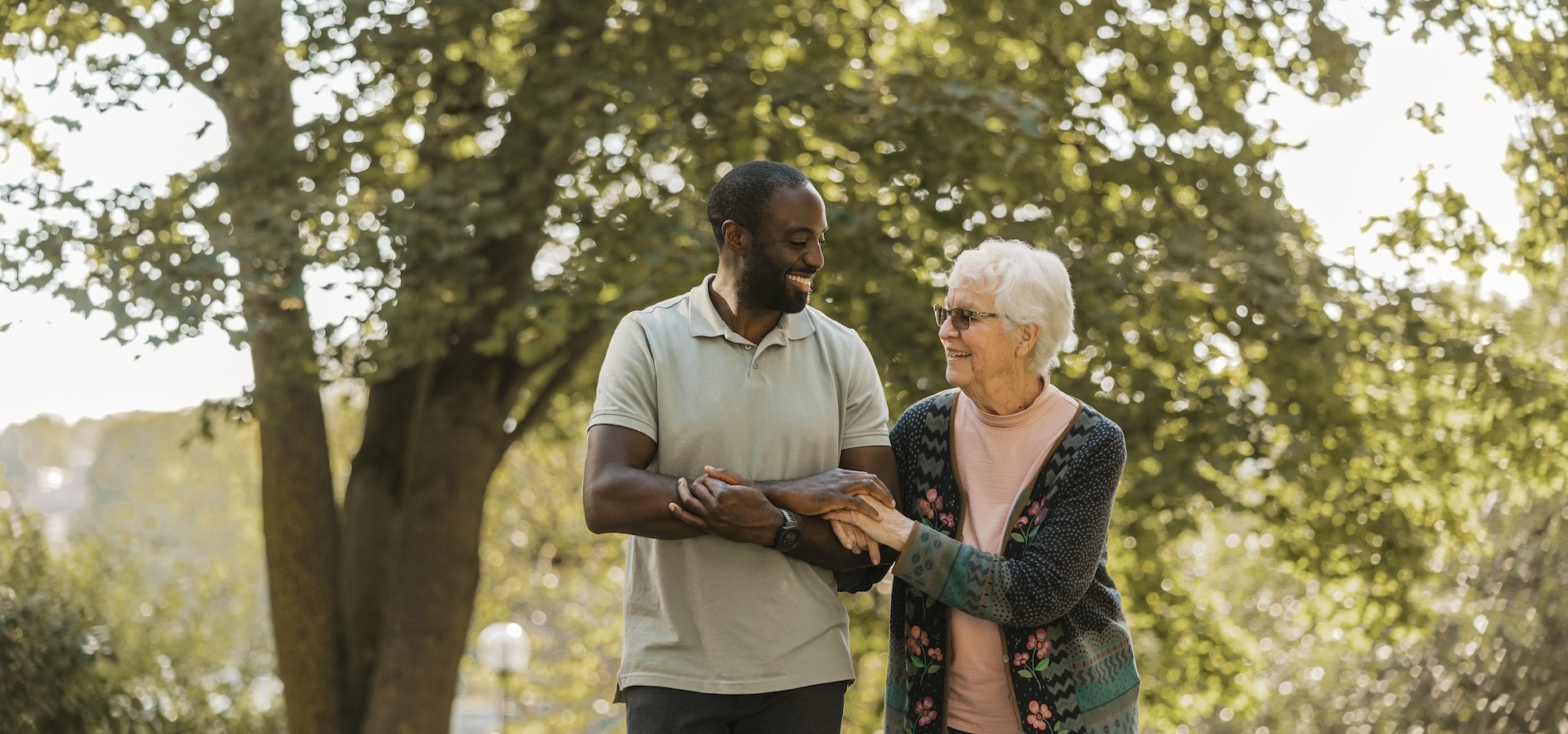Senior woman and smiling male caregiver walking in arm and arm at park