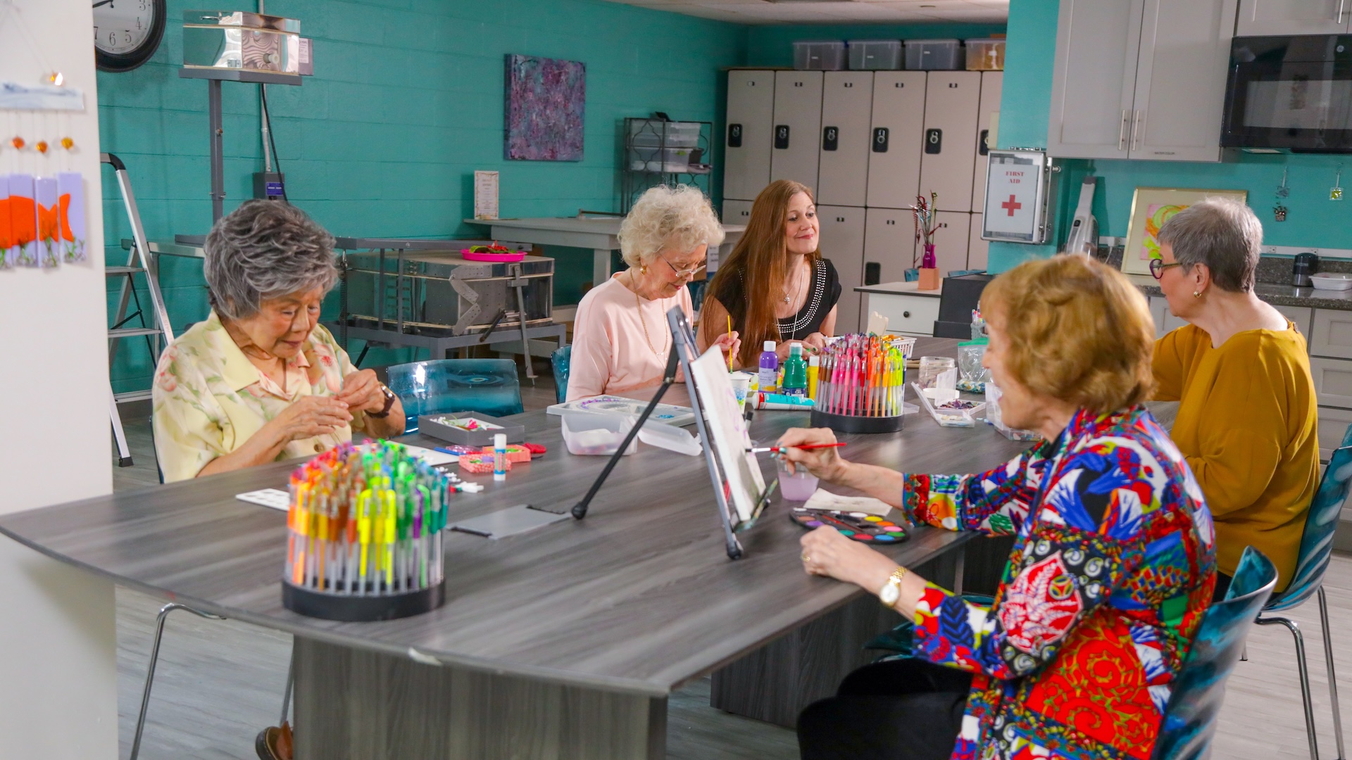 Senior women sitting around a large table in a bright art studio, engaged in painting and drawing.