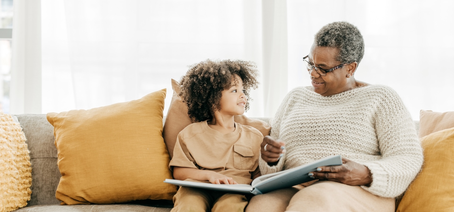 An older woman and a young child sit together on a couch, looking at an open book.
