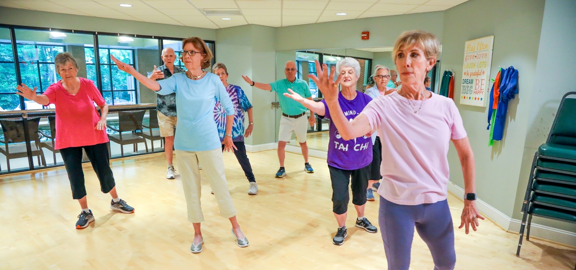 A group of seniors practicing Tai Chi movements in a bright fitness studio.