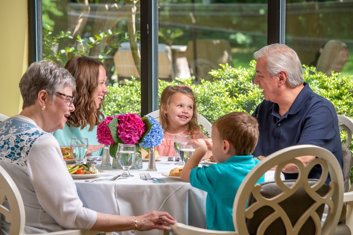 Multi-generational family smiling and talking at a dining table.